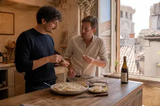 Friends sharing brandade de morue and cheese near a window in a sunlit Nîmes kitchen with glasses of red wine.