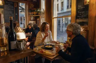Candid moment of a couple savoring traditional dishes and wine in a warmly lit, wood-paneled Chambéry bistro with locals nearby.
