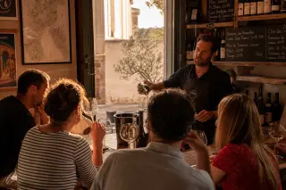 Locals and visitors sharing a wine tasting moment with a winemaker in a warmly lit wine bar, golden sunlight enhancing glasses and rustic decor.