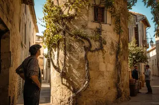 A vintner observes a historic tower in a sunlit Nîmes alley, vine branches climbing the stone, with neighbors sharing a quiet moment and harvest baskets nearby, all in warm Mediterranean light.